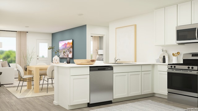 kitchen with white cabinets, a sink, light wood finished floors, stainless steel appliances, and a peninsula