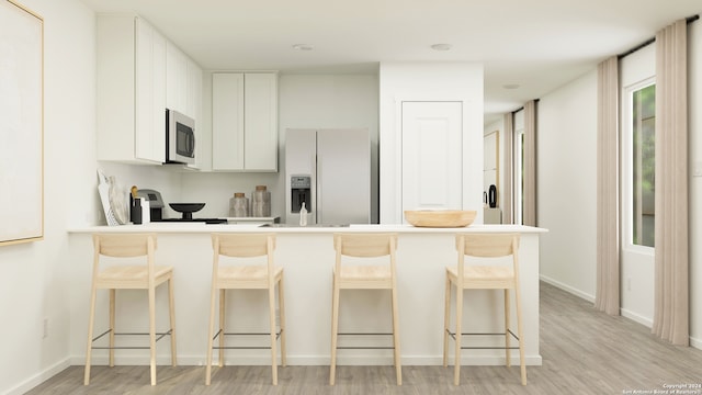 kitchen with a breakfast bar, light wood finished floors, a peninsula, stainless steel microwave, and fridge with ice dispenser