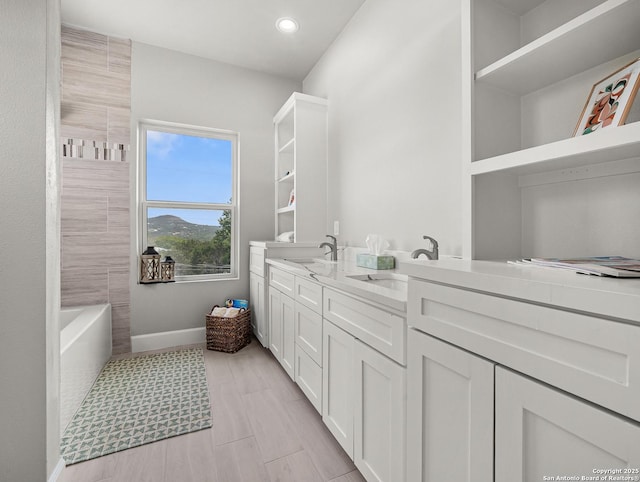 bathroom with double vanity, baseboards, a sink, and a tub to relax in