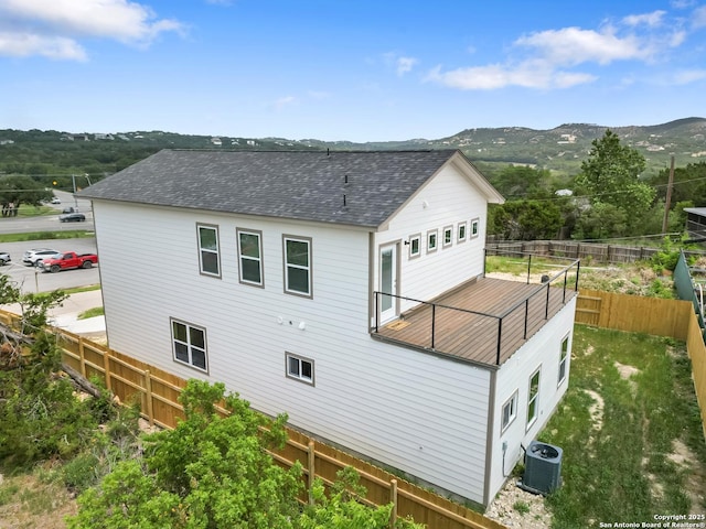 back of property with a shingled roof, a mountain view, fence, and central AC unit