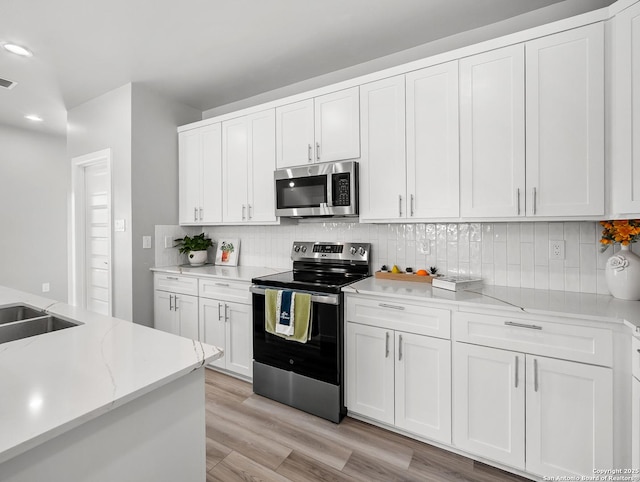 kitchen with recessed lighting, white cabinets, light wood-style flooring, appliances with stainless steel finishes, and backsplash