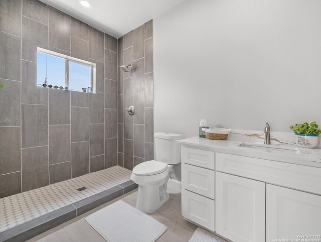 bathroom with vanity, baseboards, toilet, and tiled shower