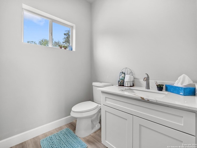 half bath with baseboards, wood finished floors, toilet, and vanity