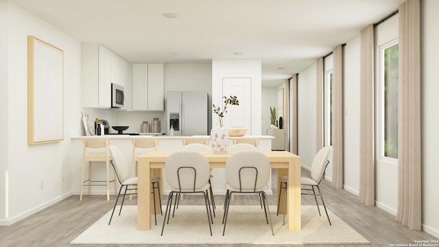 kitchen with white cabinetry, baseboards, light wood-type flooring, a kitchen bar, and refrigerator with ice dispenser