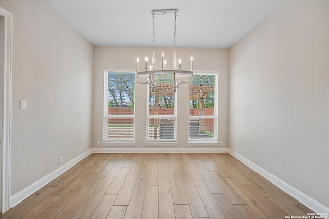 unfurnished dining area featuring baseboards, light wood-style flooring, a chandelier, and a wealth of natural light