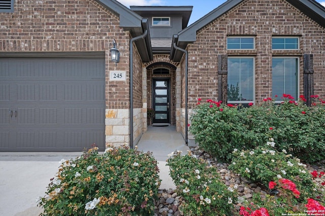 doorway to property with an attached garage, stone siding, and brick siding