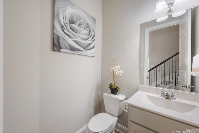 half bathroom with vanity, a textured wall, baseboards, and toilet