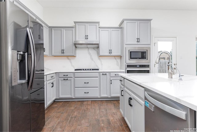 kitchen featuring dark wood-style flooring, a sink, light stone counters, under cabinet range hood, and stainless steel appliances