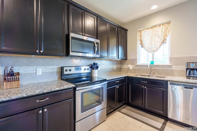 kitchen with light stone countertops, appliances with stainless steel finishes, a sink, decorative backsplash, and light tile patterned floors