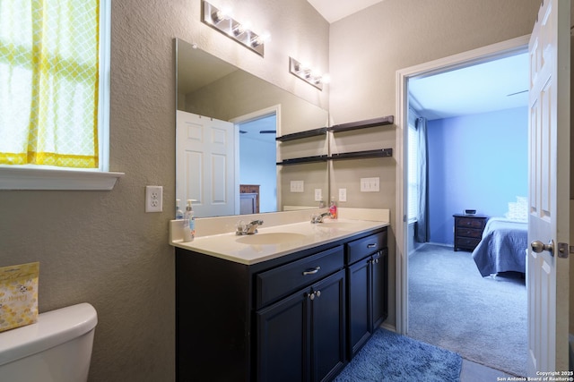 bathroom with a sink, a textured wall, toilet, and double vanity