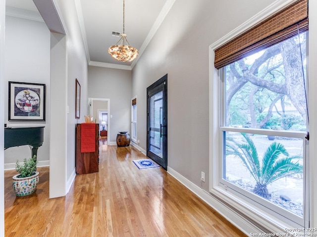 foyer entrance with visible vents, crown molding, light wood-type flooring, baseboards, and a chandelier