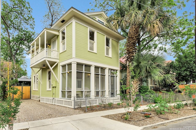 view of front facade with fence, a balcony, and a sunroom