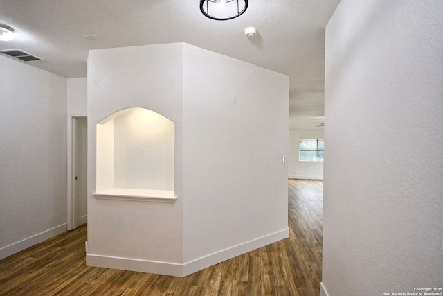 hallway with baseboards, wood finished floors, and visible vents