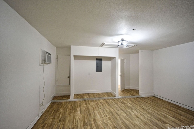 spare room with an AC wall unit, baseboards, wood finished floors, and electric panel