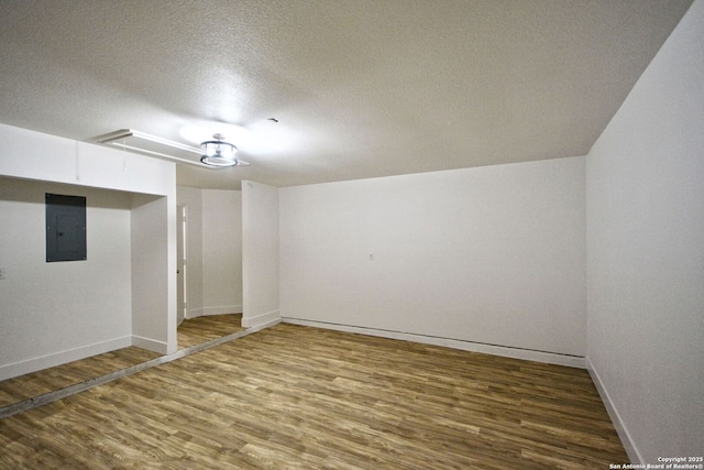 interior space featuring wood finished floors, baseboards, attic access, a textured ceiling, and electric panel