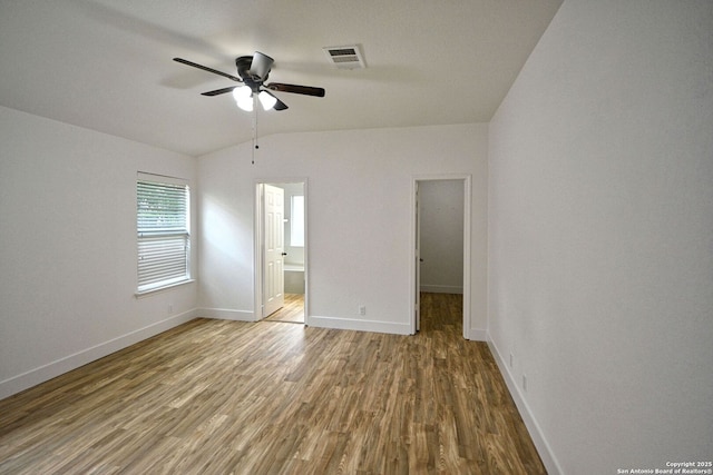 unfurnished bedroom featuring visible vents, wood finished floors, baseboards, connected bathroom, and vaulted ceiling