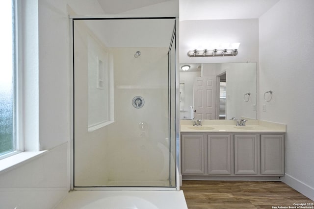 full bathroom with double vanity, a shower stall, a sink, and wood finished floors