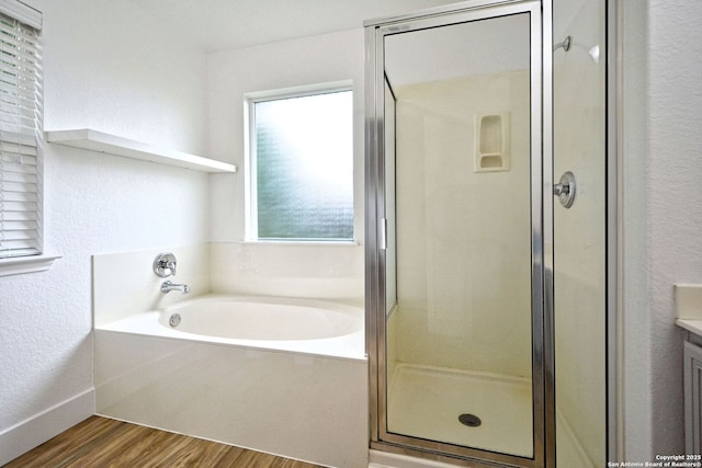 full bathroom with a textured wall, vanity, wood finished floors, a garden tub, and a stall shower