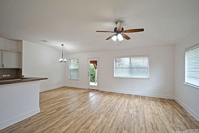 unfurnished living room with baseboards, visible vents, ceiling fan with notable chandelier, and light wood-style floors