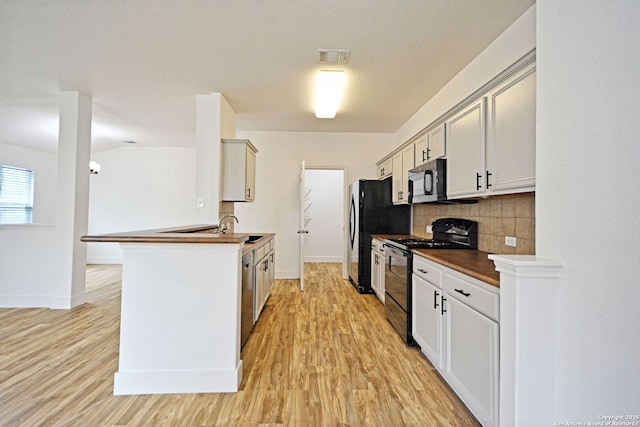 kitchen featuring decorative backsplash, dark countertops, baseboards, black appliances, and light wood finished floors