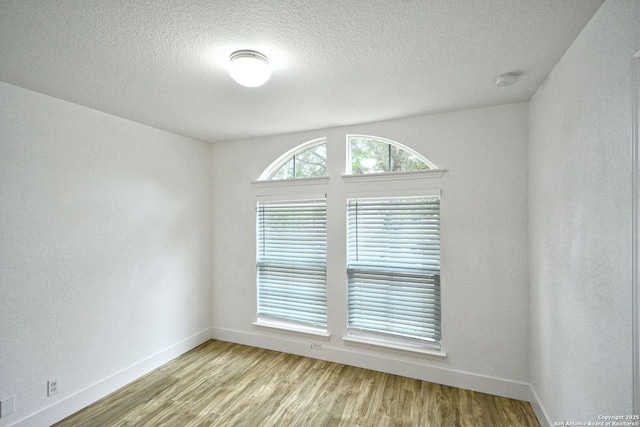 spare room featuring a textured ceiling, baseboards, and wood finished floors