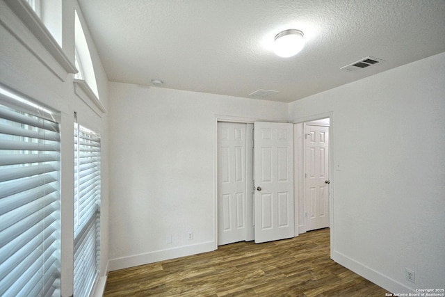 unfurnished bedroom with baseboards, a textured ceiling, wood finished floors, and visible vents