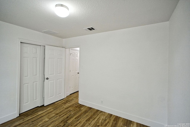 unfurnished bedroom featuring baseboards, a closet, dark wood finished floors, and visible vents