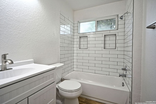 full bath featuring vanity, a textured wall, shower / bathtub combination, wood finished floors, and toilet