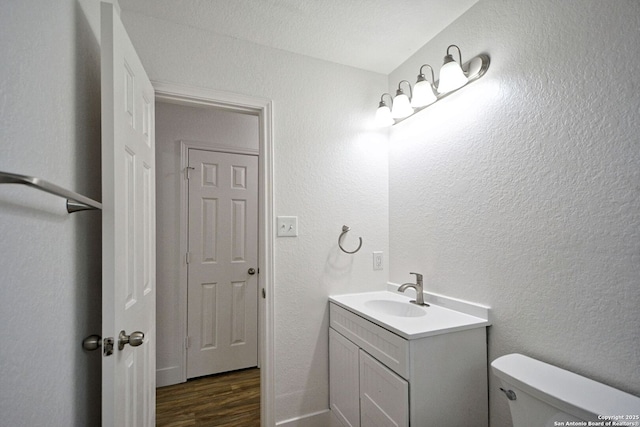 half bathroom featuring vanity, a textured wall, toilet, and wood finished floors