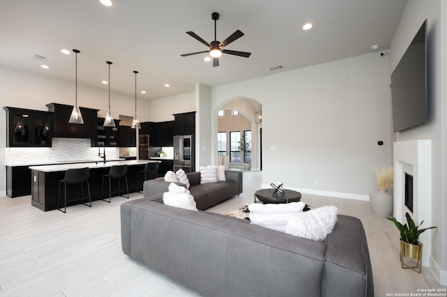 living area with visible vents, ceiling fan, a fireplace with raised hearth, arched walkways, and light wood finished floors