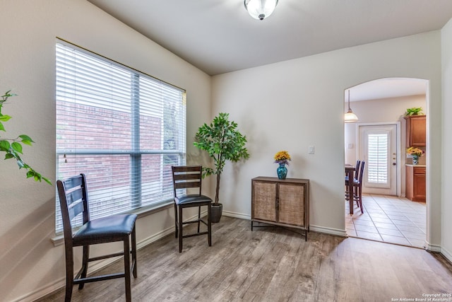living area with arched walkways, baseboards, and light wood-type flooring