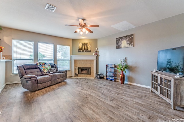 living area featuring ceiling fan, visible vents, a fireplace, wood finished floors, and baseboards