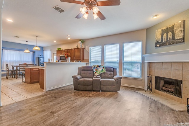 living room featuring visible vents, ceiling fan, a tiled fireplace, and light wood-type flooring