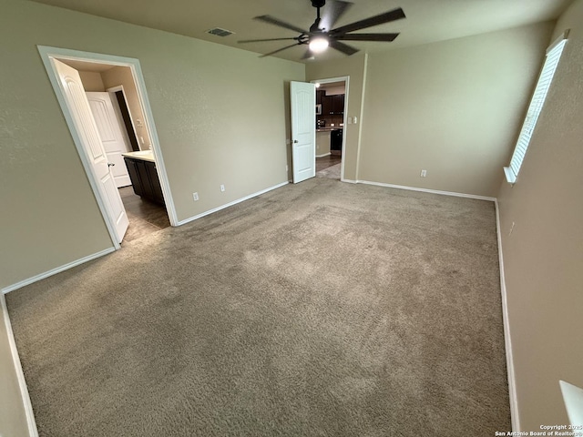 unfurnished bedroom featuring ensuite bath, carpet, a ceiling fan, baseboards, and visible vents