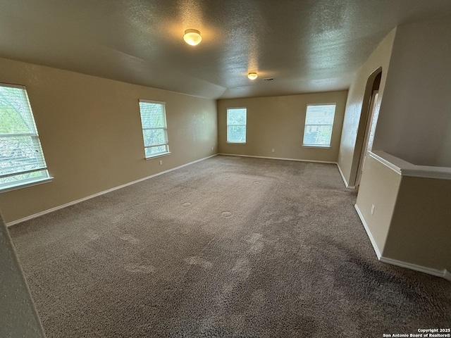 carpeted spare room featuring arched walkways, baseboards, and a textured ceiling