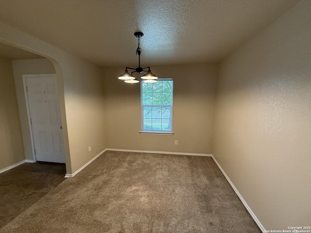 spare room with baseboards, dark carpet, a textured ceiling, a chandelier, and arched walkways