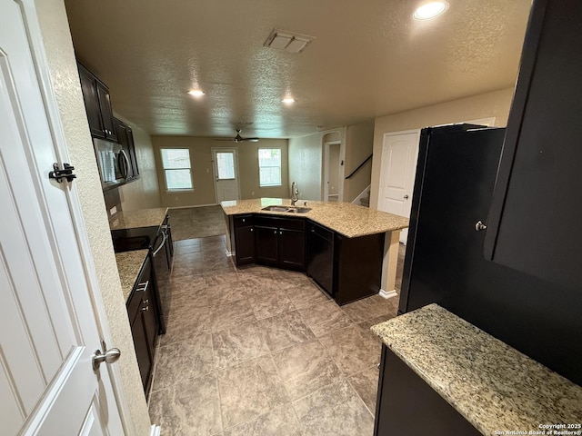 kitchen featuring a textured ceiling, visible vents, a sink, black appliances, and an island with sink