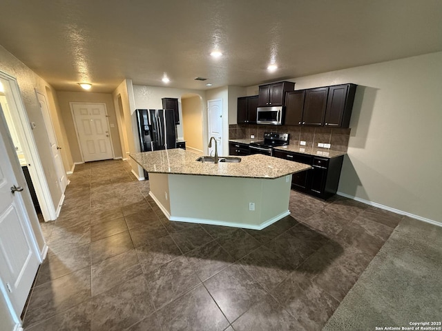 kitchen with appliances with stainless steel finishes, a sink, arched walkways, an island with sink, and backsplash