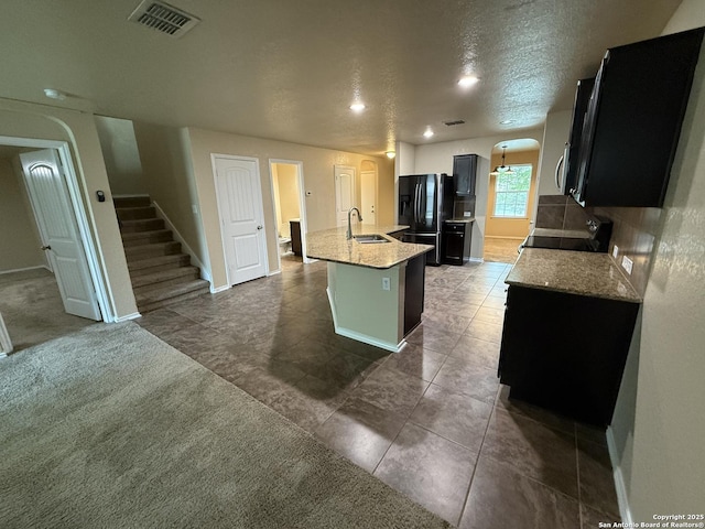 kitchen with a sink, a kitchen island with sink, black refrigerator with ice dispenser, stove, and visible vents