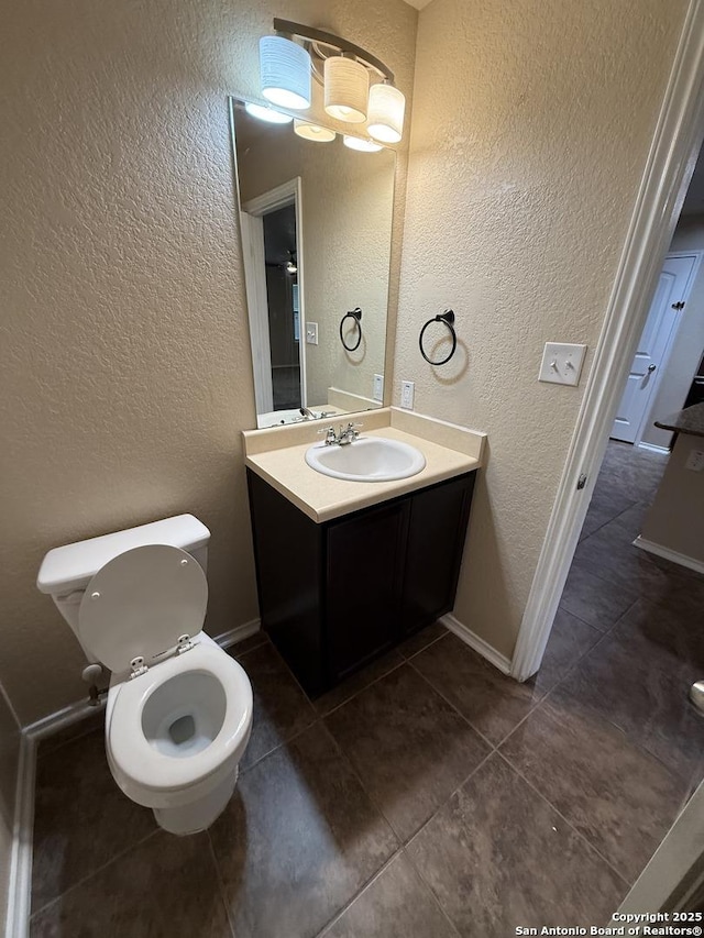 bathroom with a textured wall, vanity, toilet, tile patterned floors, and baseboards