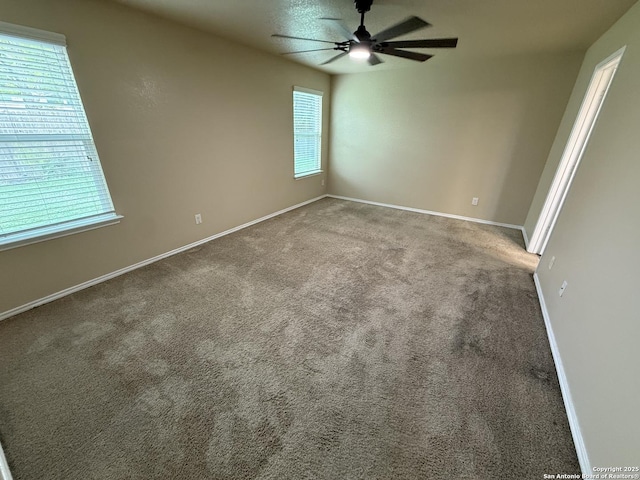 carpeted spare room with a healthy amount of sunlight, baseboards, and a ceiling fan