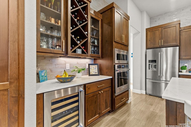 bar with decorative backsplash, wine cooler, light wood-style floors, baseboards, and stainless steel appliances