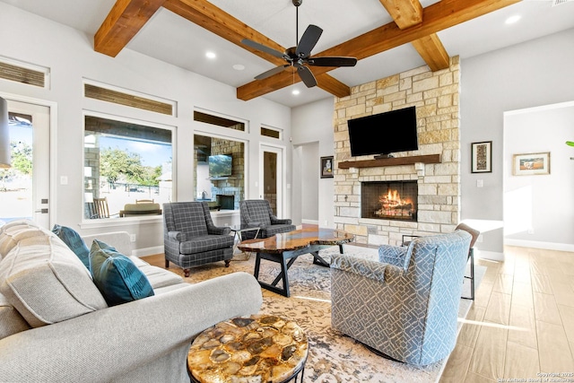 living room with a stone fireplace, baseboards, ceiling fan, and beamed ceiling
