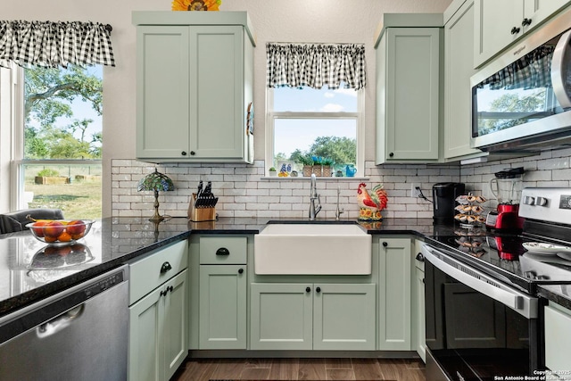 kitchen with wood finished floors, green cabinetry, tasteful backsplash, a sink, and stainless steel appliances