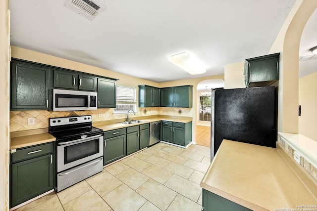 kitchen featuring visible vents, light countertops, green cabinetry, arched walkways, and appliances with stainless steel finishes