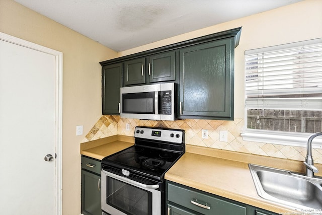 kitchen with decorative backsplash, appliances with stainless steel finishes, a sink, light countertops, and green cabinets