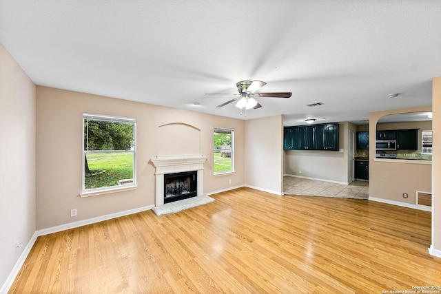 unfurnished living room featuring a ceiling fan, visible vents, a healthy amount of sunlight, and light wood-style flooring