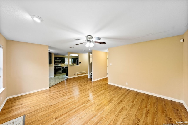 unfurnished living room featuring stairway, baseboards, a ceiling fan, and light wood-type flooring