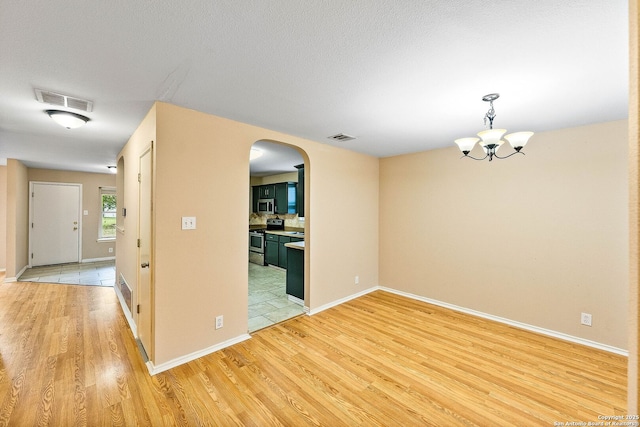 spare room featuring visible vents, arched walkways, light wood-style flooring, and a notable chandelier