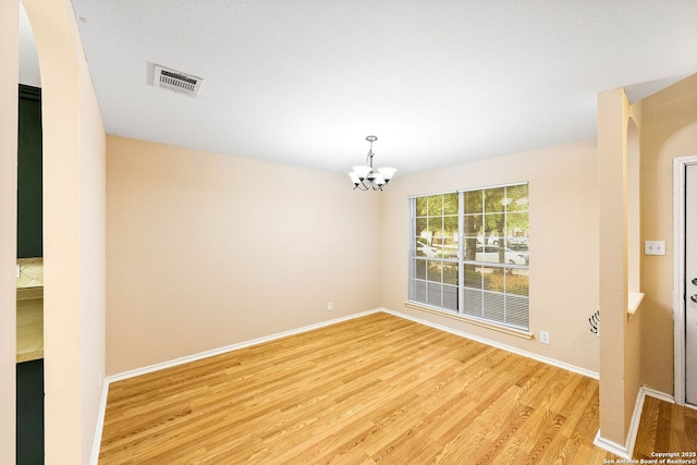 empty room featuring visible vents, arched walkways, light wood-type flooring, baseboards, and a chandelier